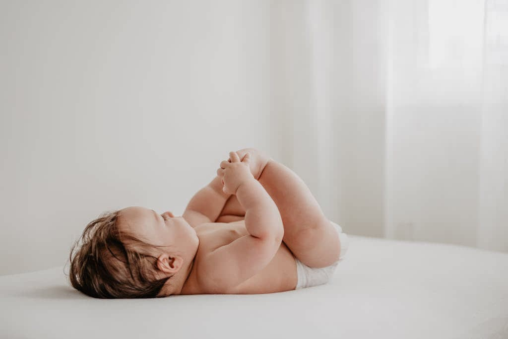 A baby in a diaper in happy baby yoga pose