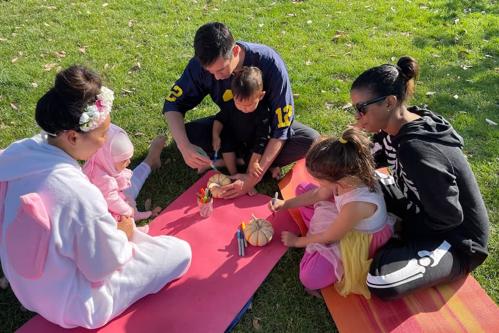 3 families in Halloween costumes in a park doing a yoga craft