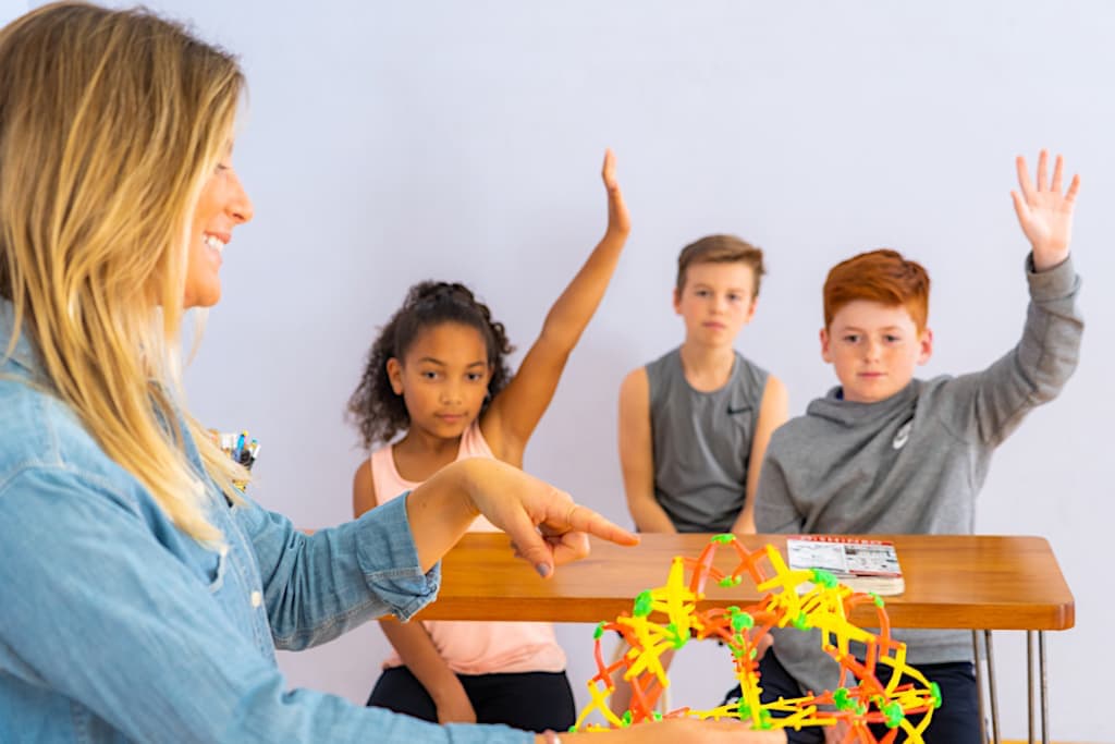 A teacher pointing to an Hoberman sphere with children raising their hands