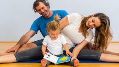 A family doing yoga with their toddler reading a yoga book